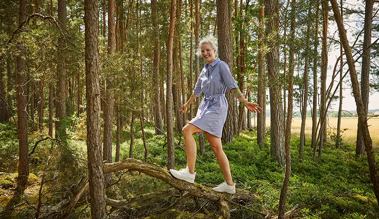 Frau balanciert auf einem umgestürzten Baum im Wald. 