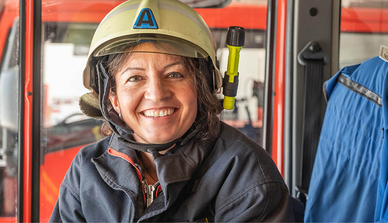 Porträtfoto: Andrea Fürstberger mit Helm und Einsatzjacke in einem Feuerwehrfahrzeug. Sie lacht in die Kamera.