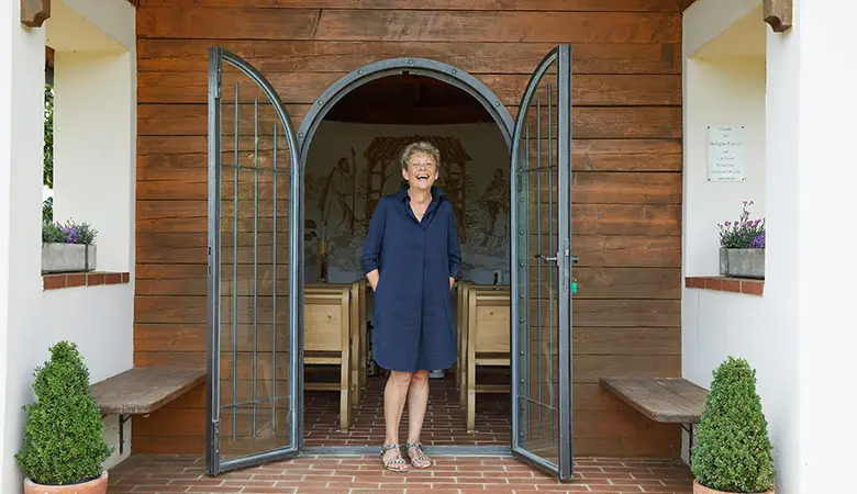 Frau steht vor dem Eingang einer Kapelle und lächelt.
