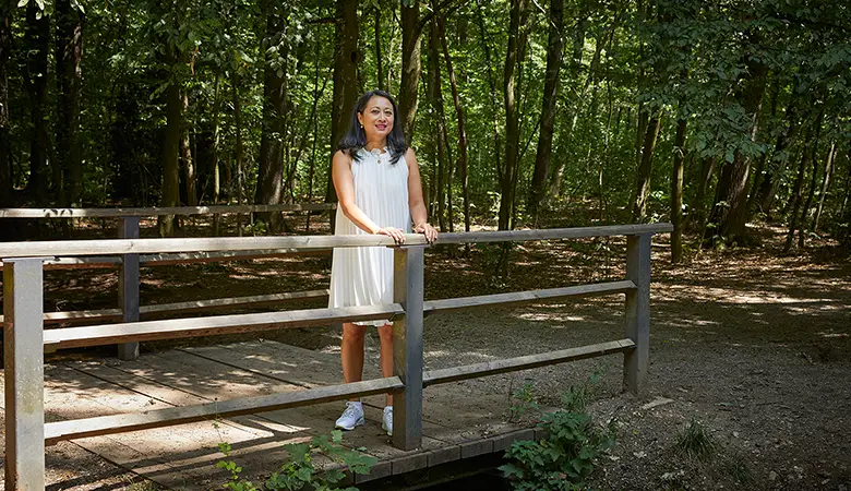 Frau im Sommerkleid steht an Brücke im Wald